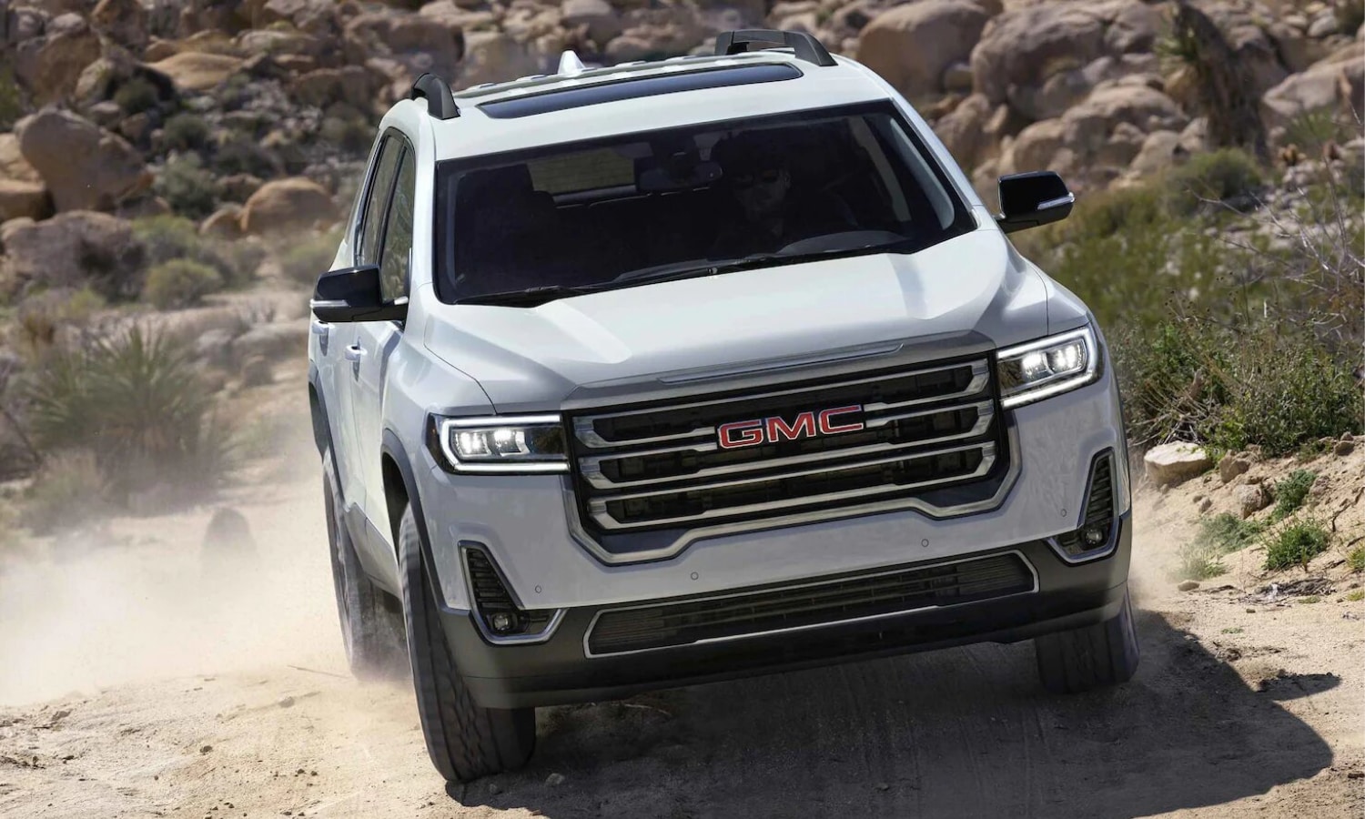 2022 GMC Acadia AT4 off-road trim in white exterior color driving down a sloped hill on a dirt road