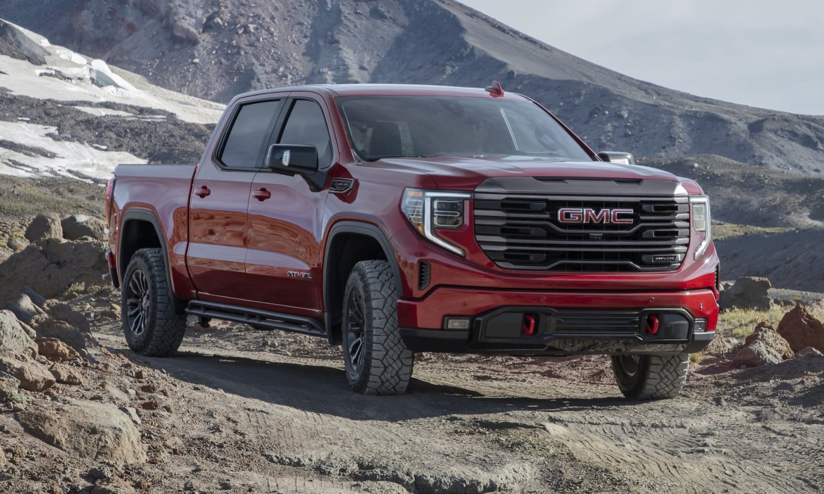 New 2022 GMC Sierra 1500 AT4 model in Cayenne Red on an off-road trail through a mountain pass