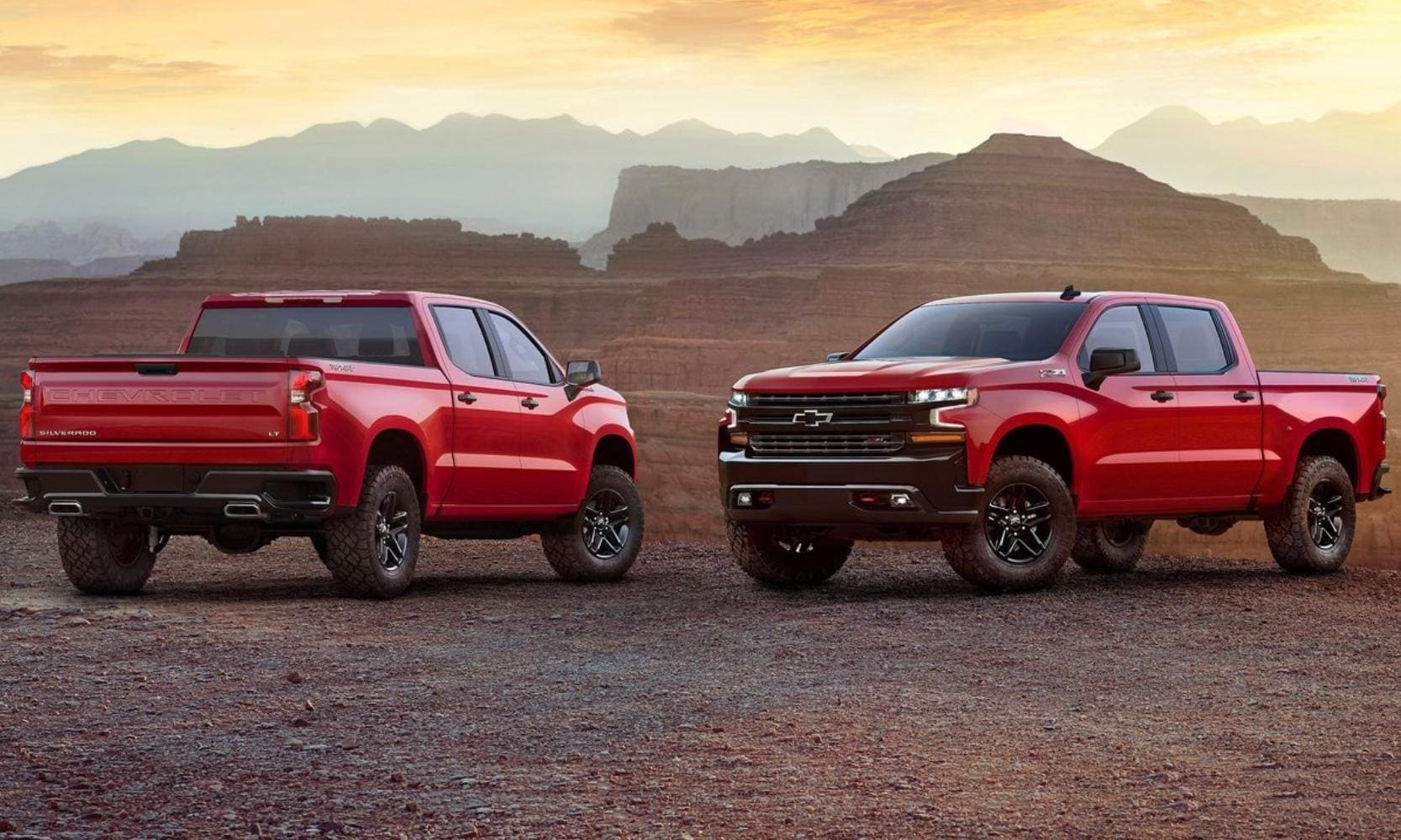 Two red Chevrolet Silverado 1500 trucks parked side by side on a desert cliff