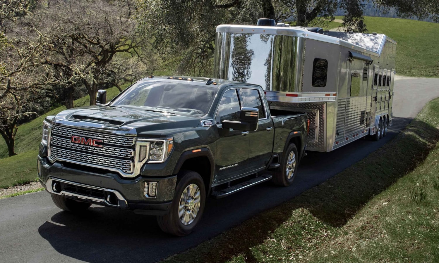 Image of a new 2022 GMC Sierra 2500HD Denali truck towing a large trailer around a curvy highway