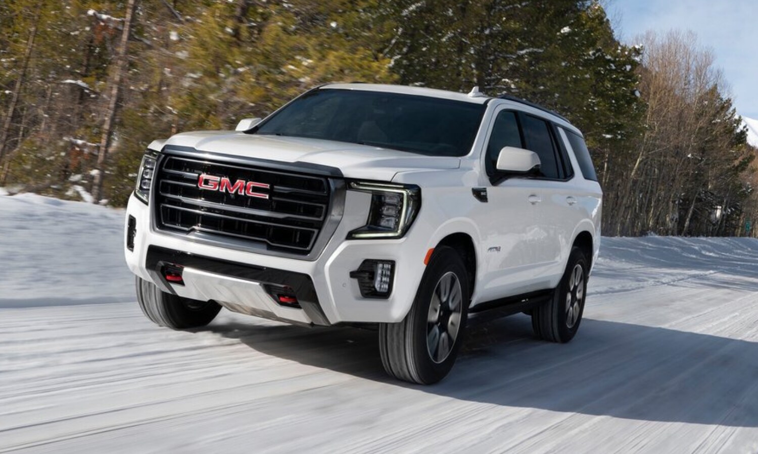 White 2022 GMC Yukon AT4 model showing off engine performance and off-road prowess driving through a forest full of snow