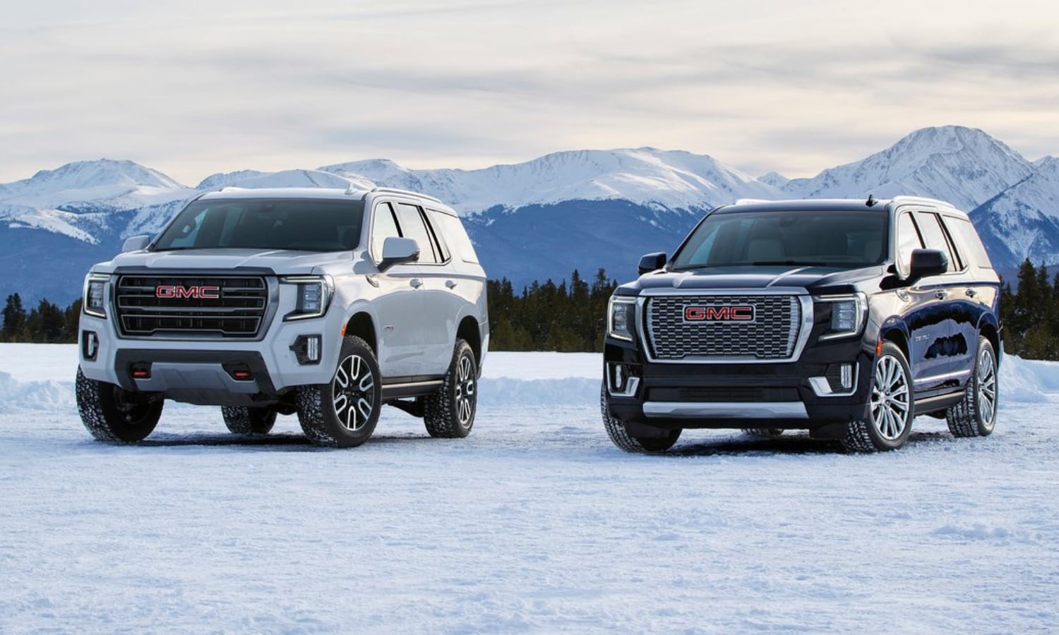 Picture of a 2022 GMC Yukon AT4 trim in white color on the left parked beside a 2022 GMC Yukon Denali trim in black color on the right