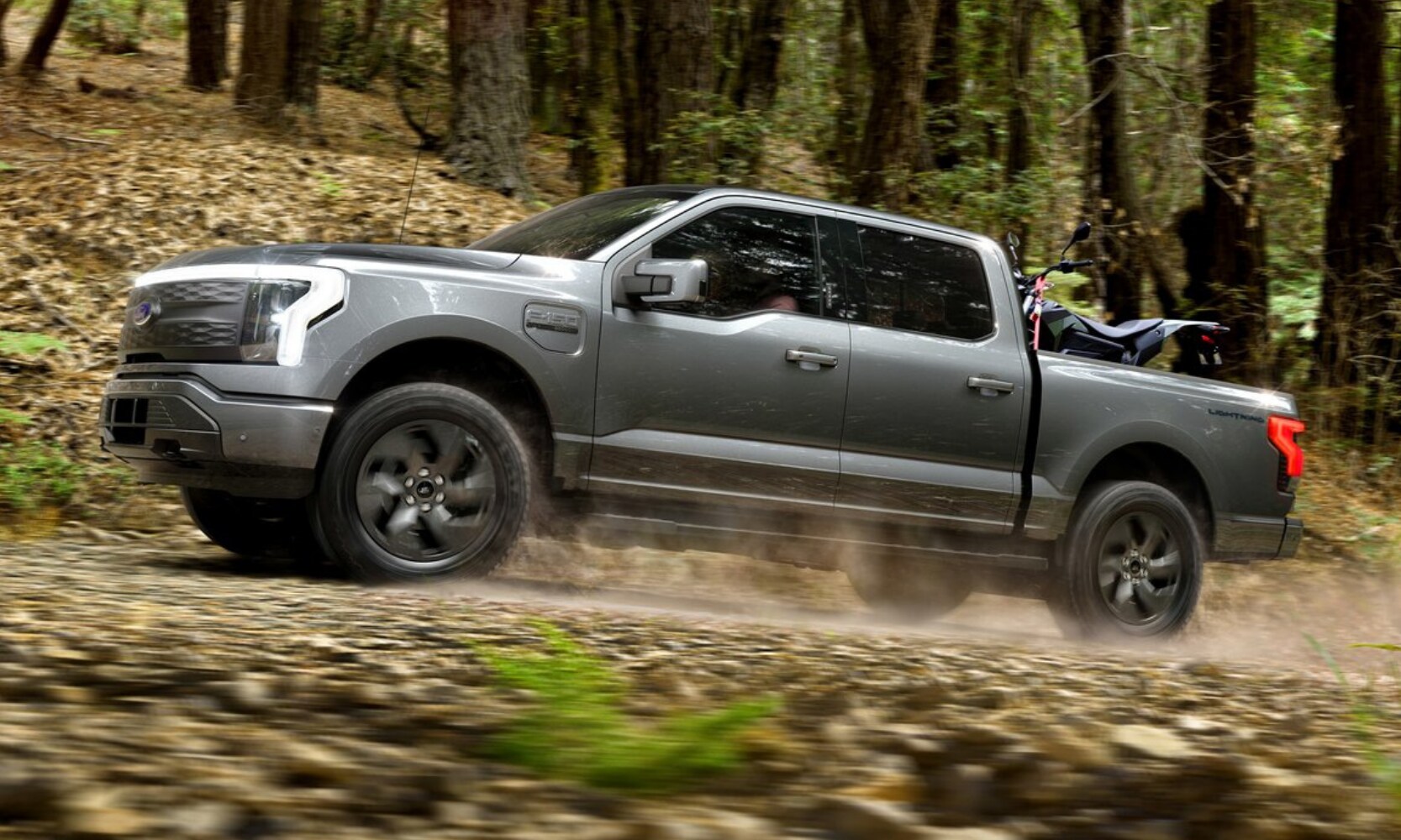 Driver side view of a 2022 Ford F-150 Lightning driving through a forest