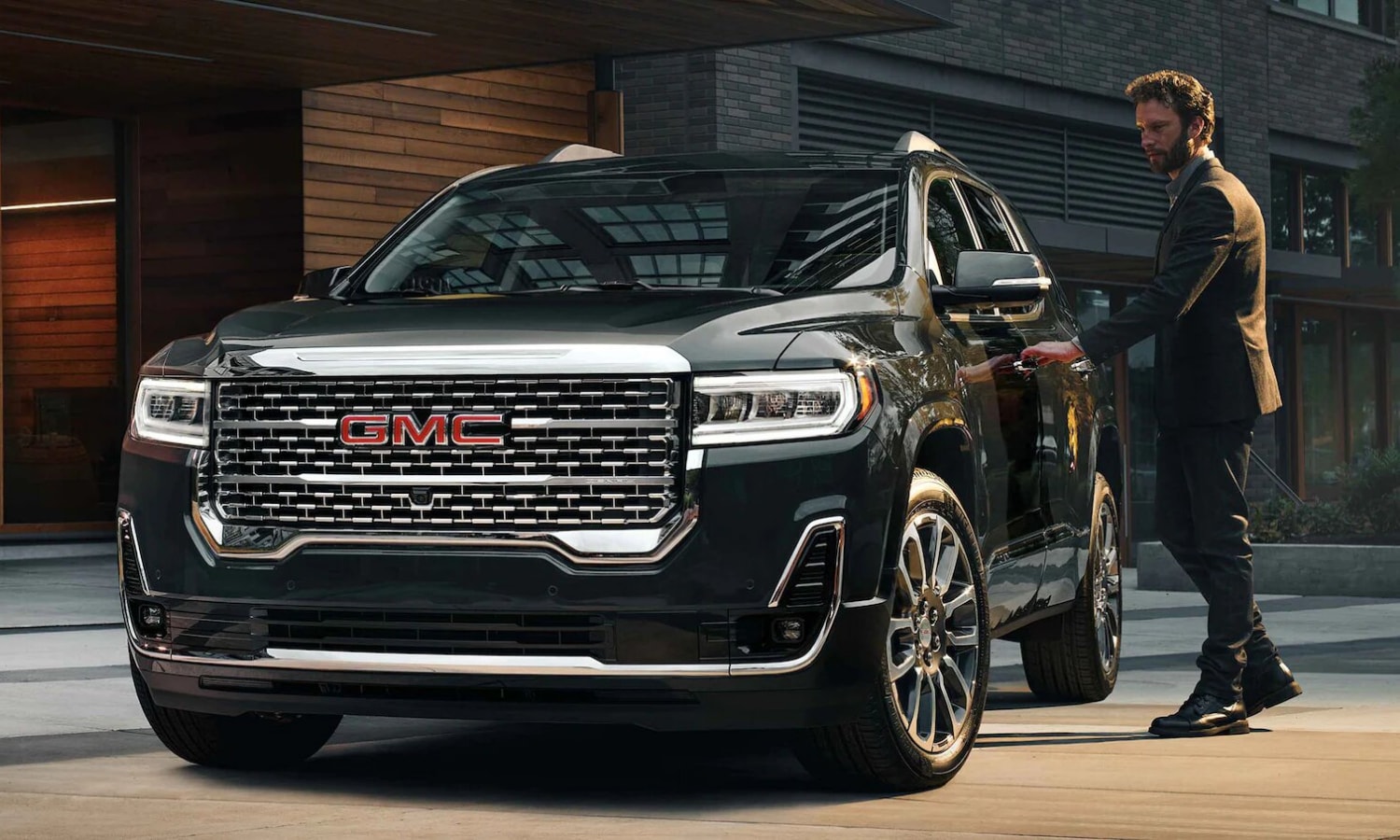 Front exterior view of the luxurious 2022 GMC Acadia Denali trim as the driver opens the door to get inside the SUV