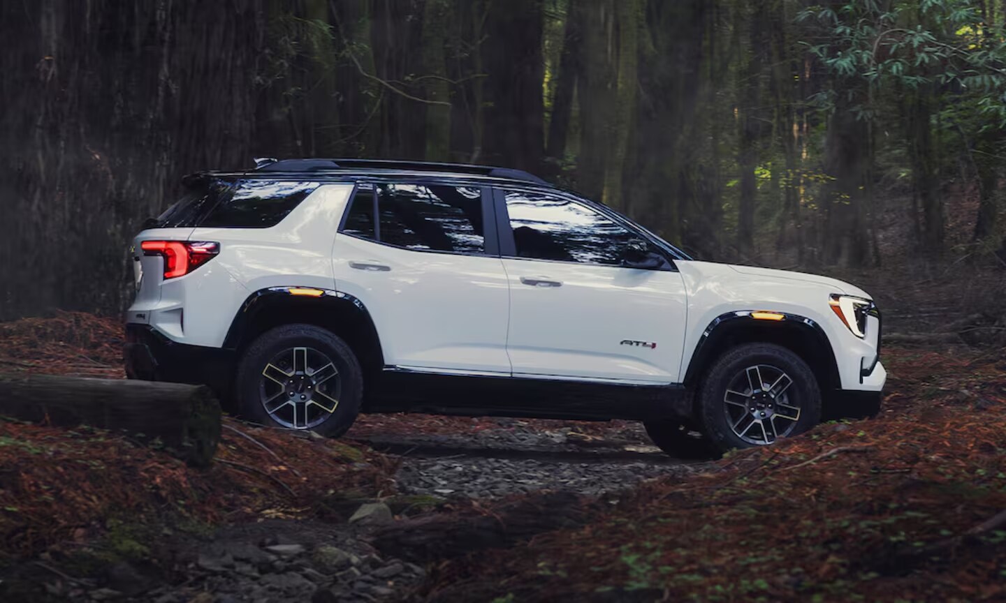 Exterior side image of a white 2026 GMC Terrain AT4 off-roading through a forest