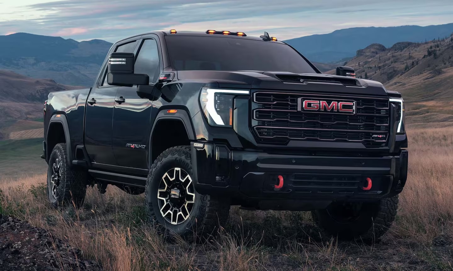 Closeup front exterior image of a black 2026 GMC Sierra HD AT4X parked in a grassy mountain field