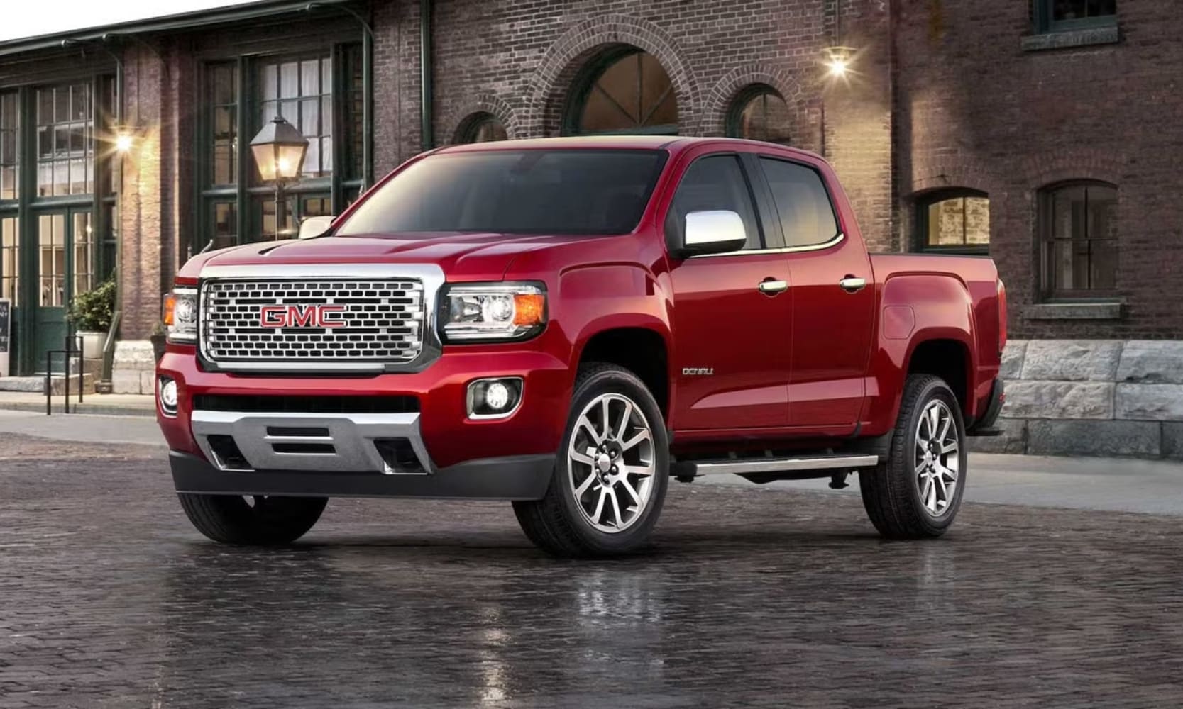 Exterior side angle image of a red 2020 GMC Canyon Denali parked in a city street in front of a building