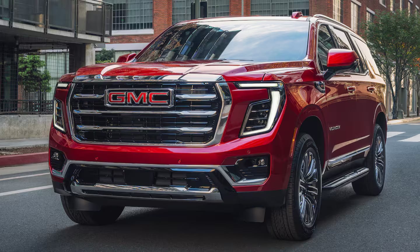 Exterior front-view image of a red 2026 GMC Yukon Elevation driving on a city street