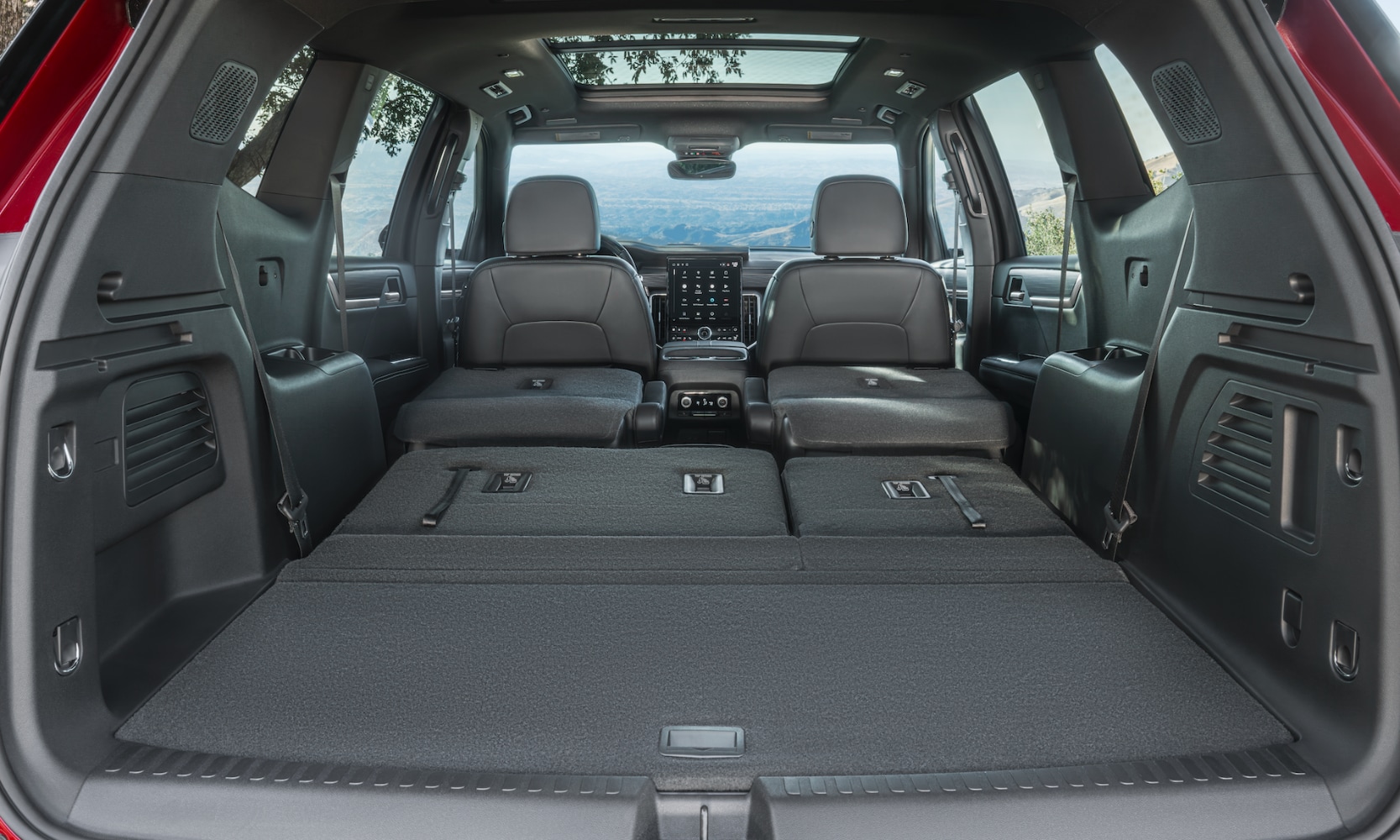 Interior image of a red 2024 GMC Acadia open trunk space with two seat rows folded down