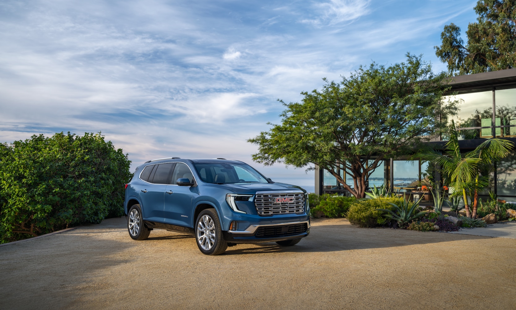 Exterior side angle image of a blue 2024 GMC Acadia Denali parked on a coastal home driveway