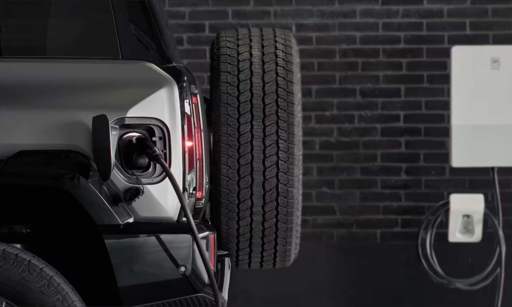 Closeup exterior rear side image of a 2026 GMC Hummer EV SUV charging inside a home