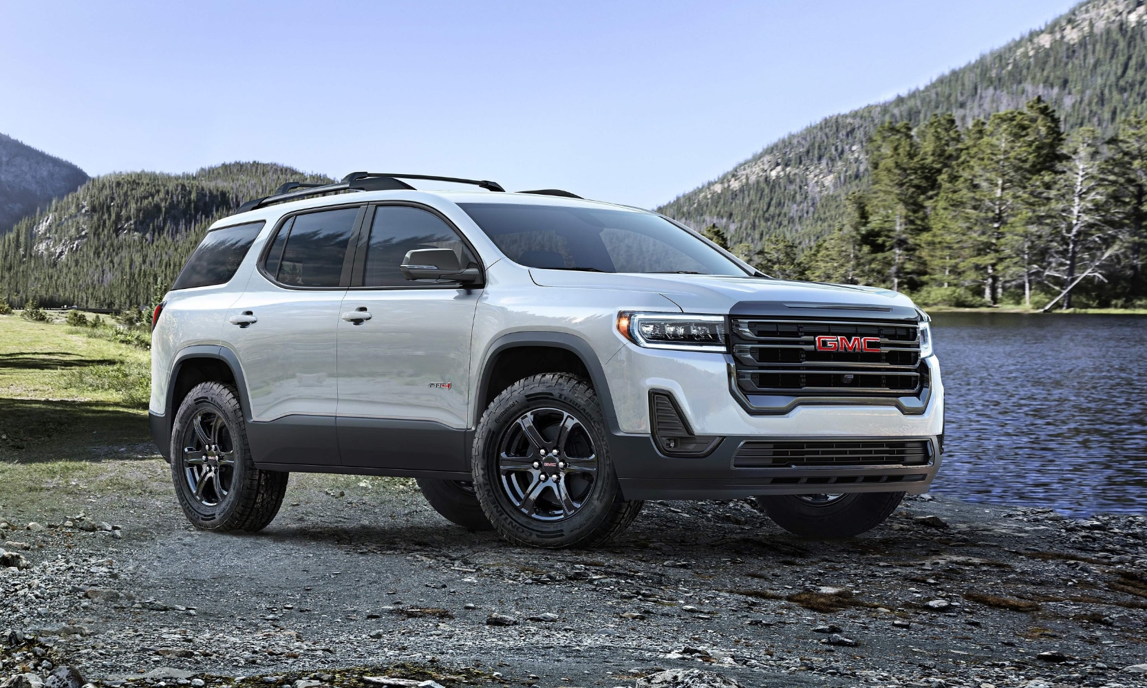 Exterior side image of a white 2020 GMC Acadia AT4 parked in front of a waterside mountain