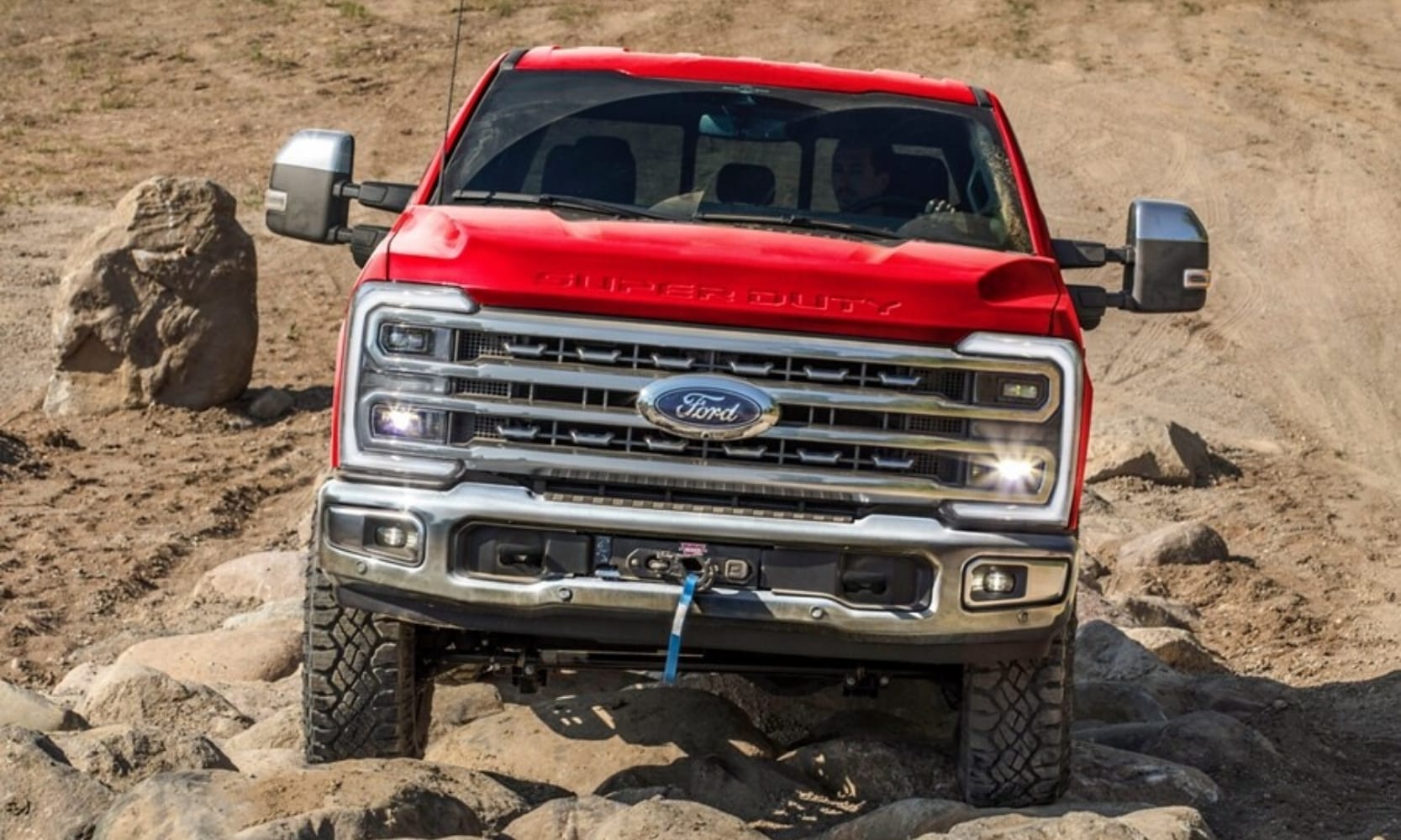 Exterior front-view image of a red 2025 Ford F-250 Super Duty TREMOR off-roading up a rocky incline