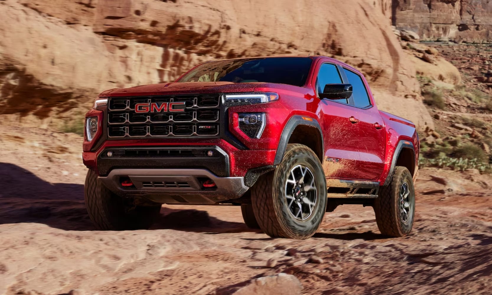 Exterior image of a red 2024 GMC Canyon AT4 parked on a rocky mountain during the day