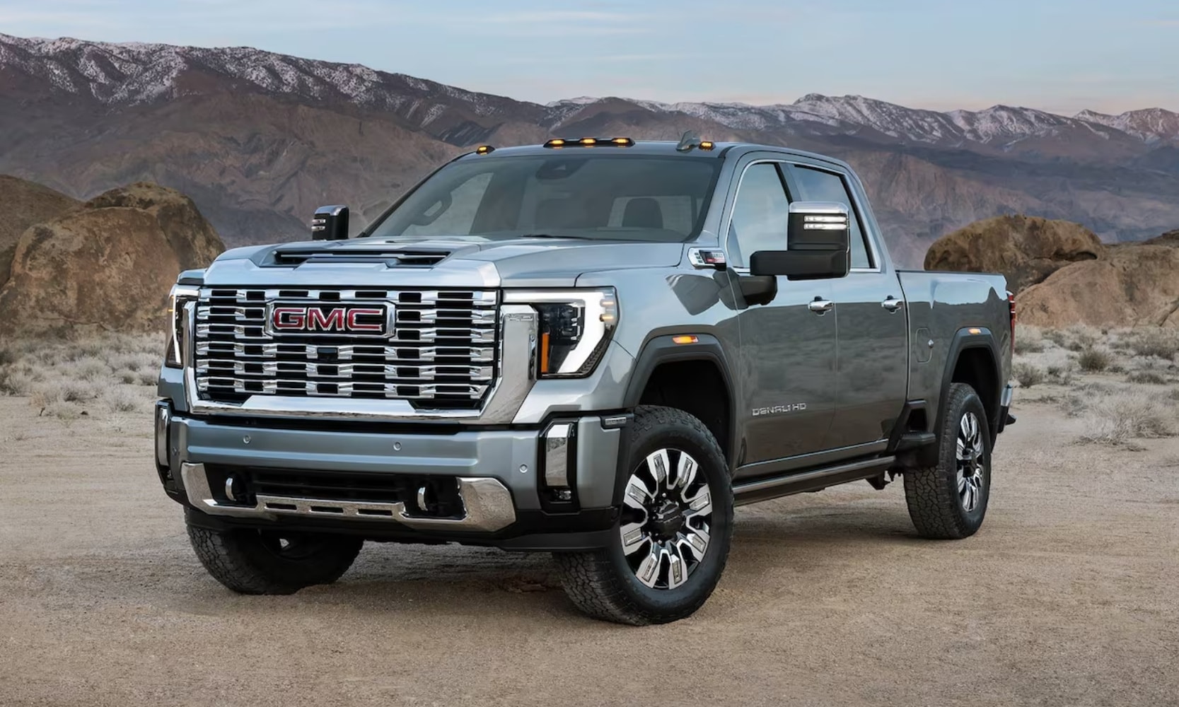 Exterior image of a light gray 2025 GMC Sierra 2500 HD Denali parked in a mountainous landscape