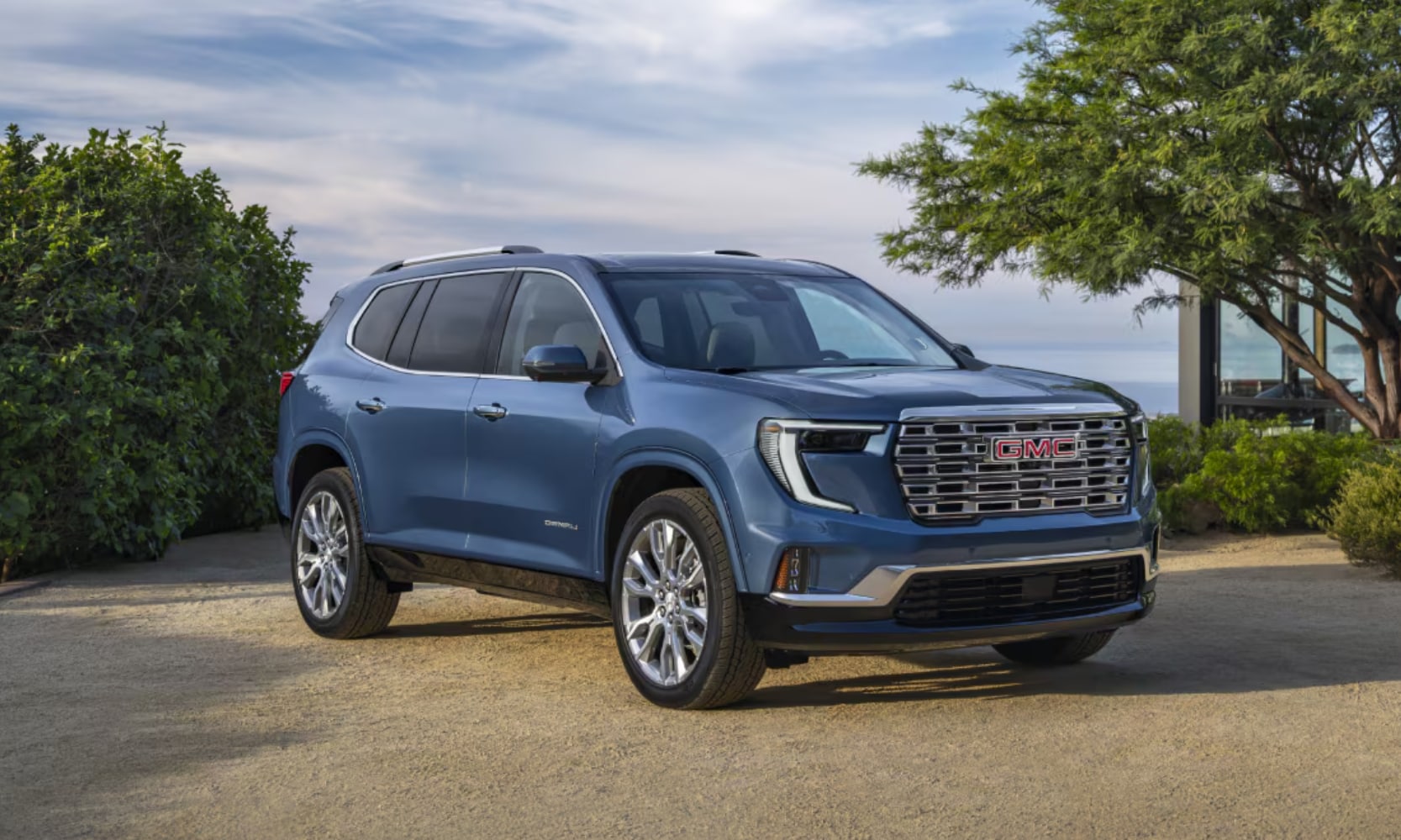 Exterior image of a blue 2025 GMC Acadia parked in a lakefront setting from a front side angled view