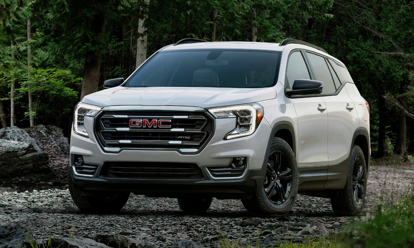 Exterior front image of a white 2022 GMC Terrain AT4 parked on a rocky trail in a forest