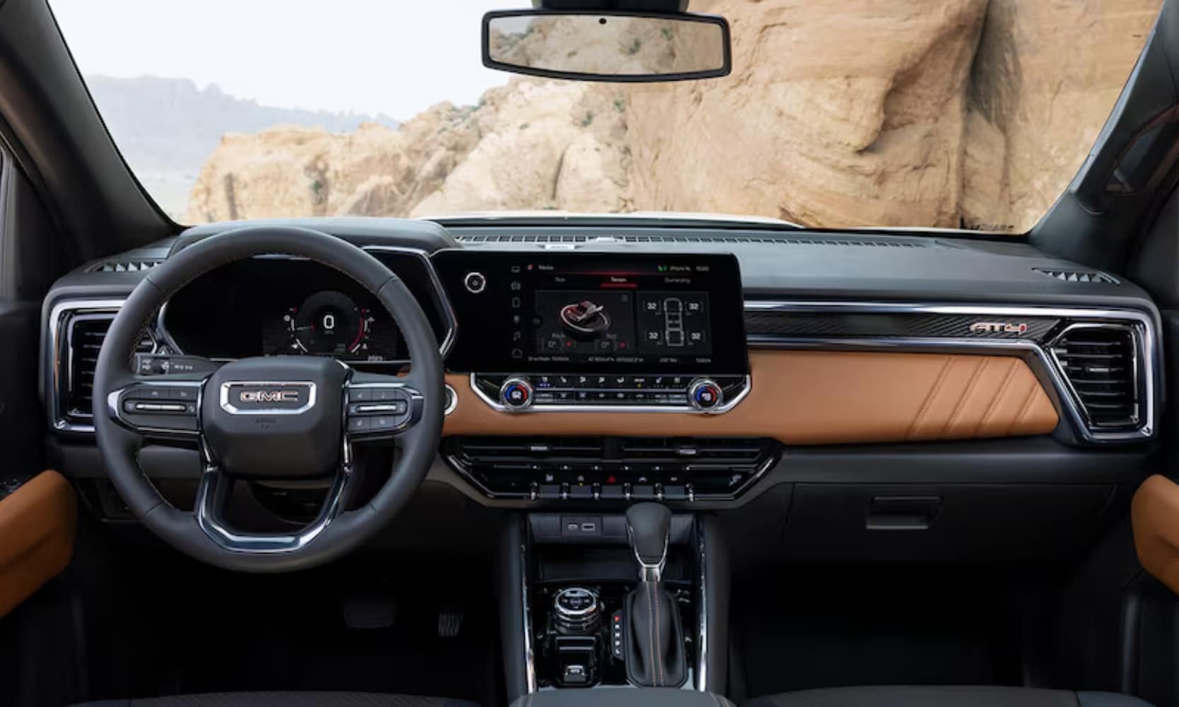 interior image of the 2024 GMC Cayon AT4's front seat perspective with a black and brown dashboard and mountain views