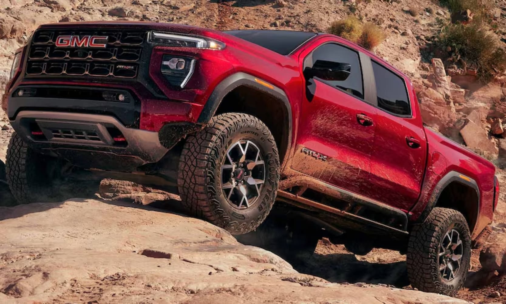 Exterior side image of a red 2024 GMC Canyon AT4X driving up a steep rocky incline