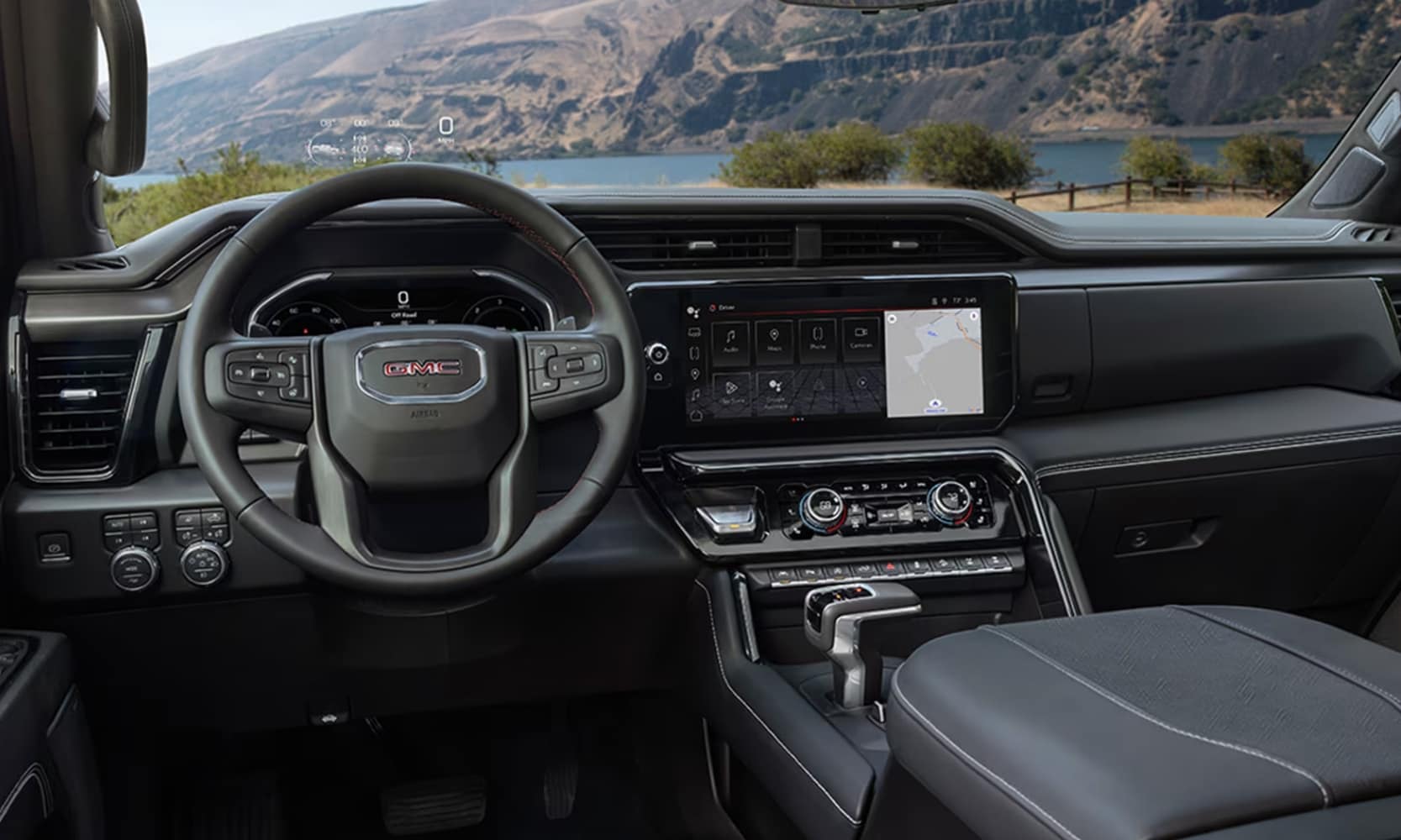 Interior image of a 2025 GMC Sierra 1500 AT4X of the front seats and dashboard in a mountain lakeside landscape