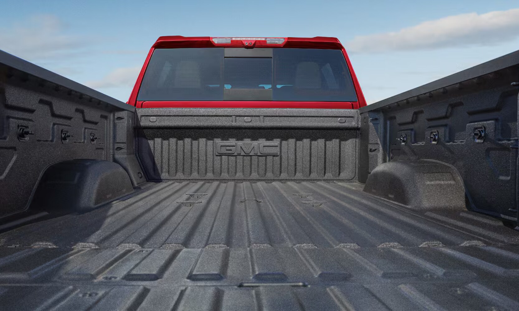 Closeup rear-view exterior image of a red 2026 GMC Sierra HD opened cargo bed
