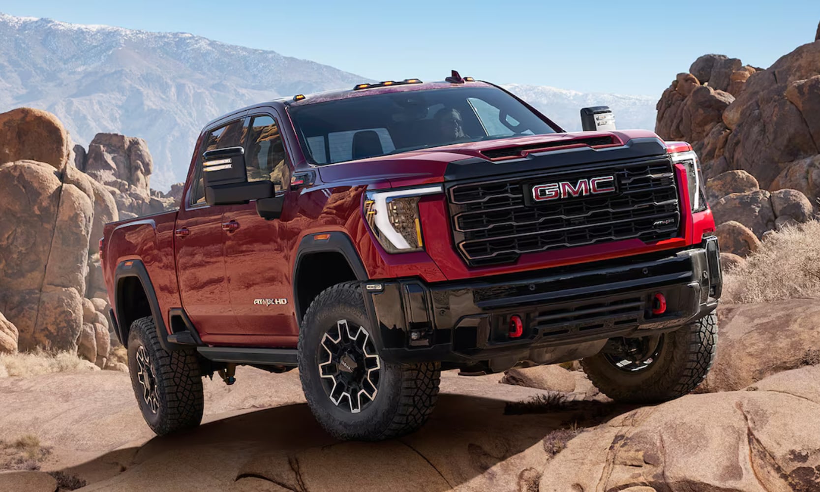 Exterior front angle image of a red 2026 GMC Sierra HD AT4X parked on a steep rocky mountain