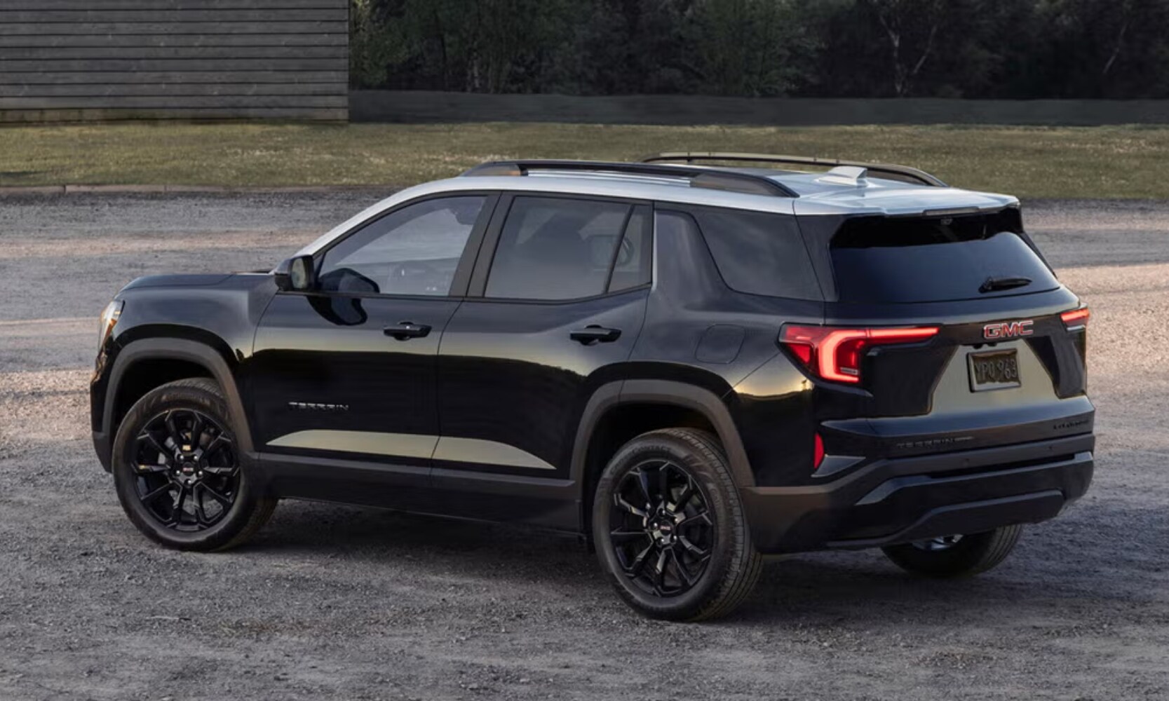 Exterior image of a black 2025 GMC Terrain Elevation parked on a gravel road from a side rear angle view