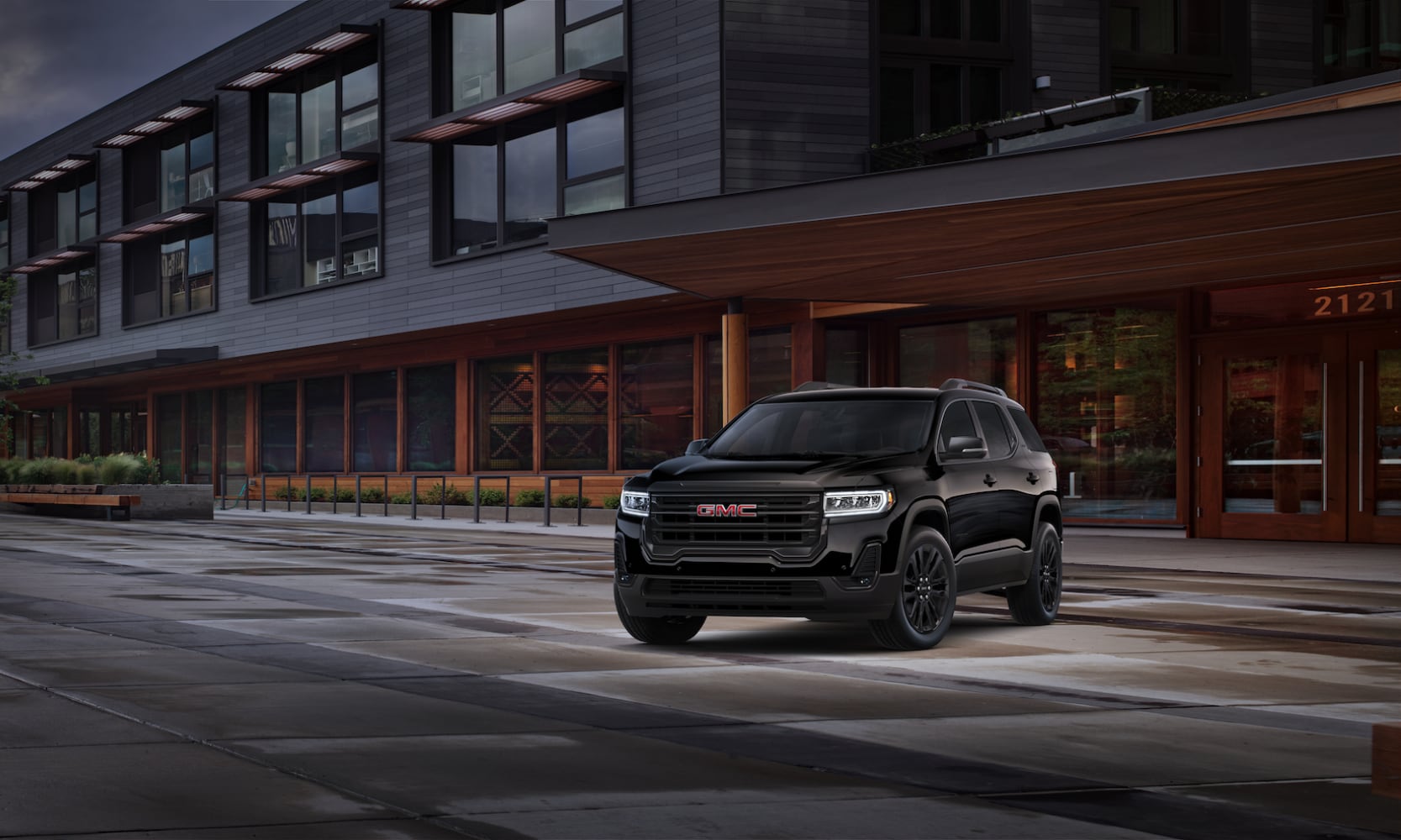 Exterior front angle image of a 2022 GMC Acadia SLT Elevation Edition parked in front of a modern building