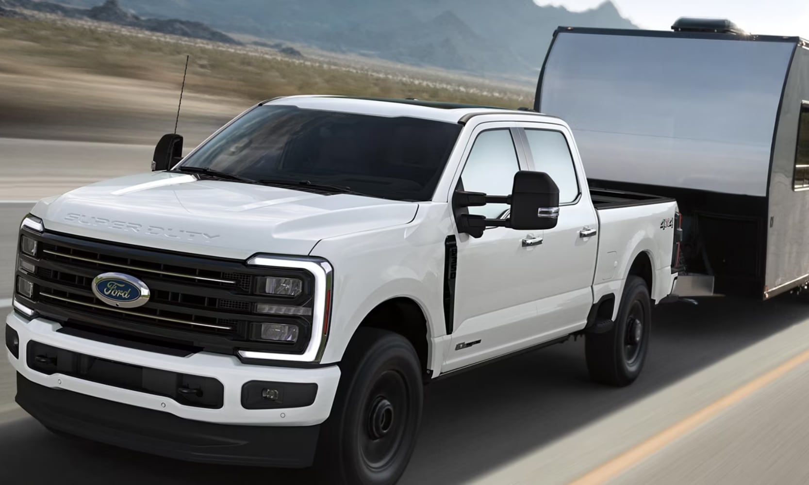 Exterior image of a white 2025 Ford F-250 Super Duty towing a camping trailer on a road with mountains in the background