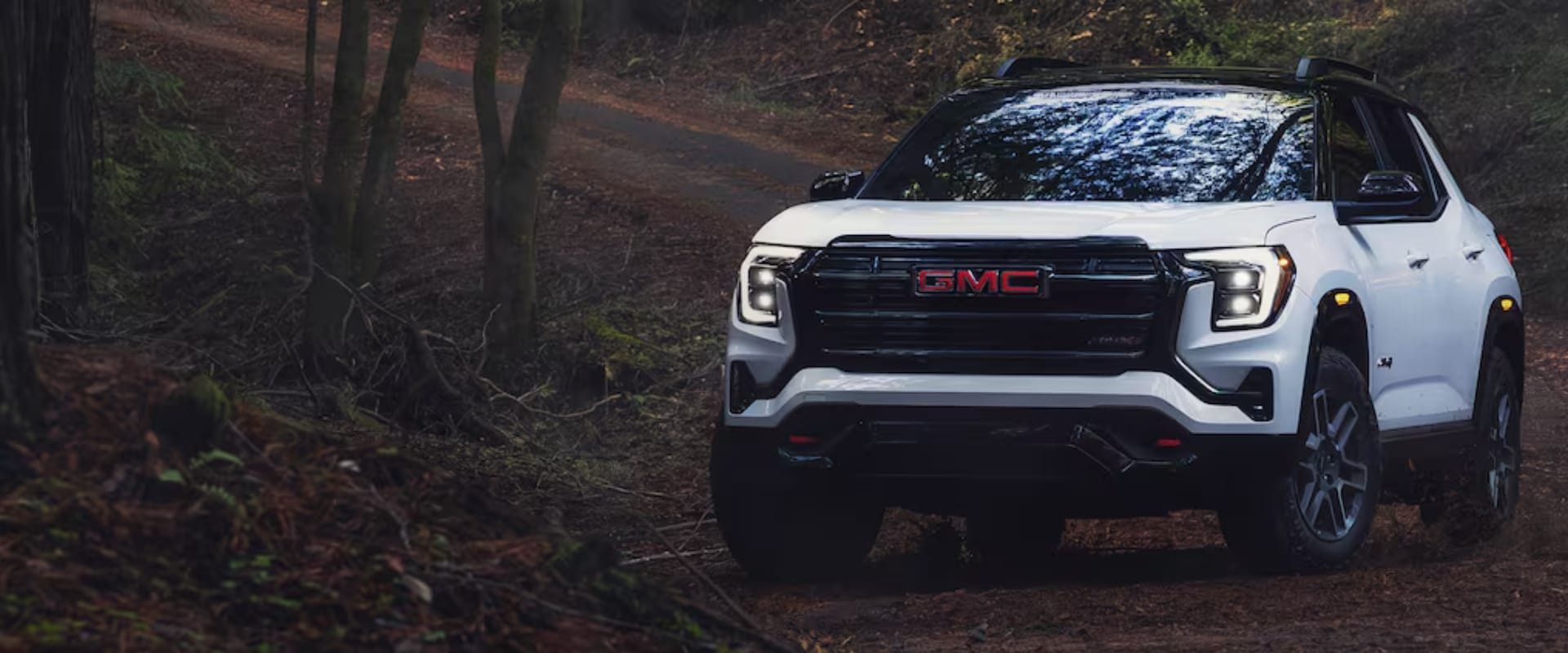 Exterior front hero image of a white 2026 GMC Terrain AT4 on a dirt road in the woods