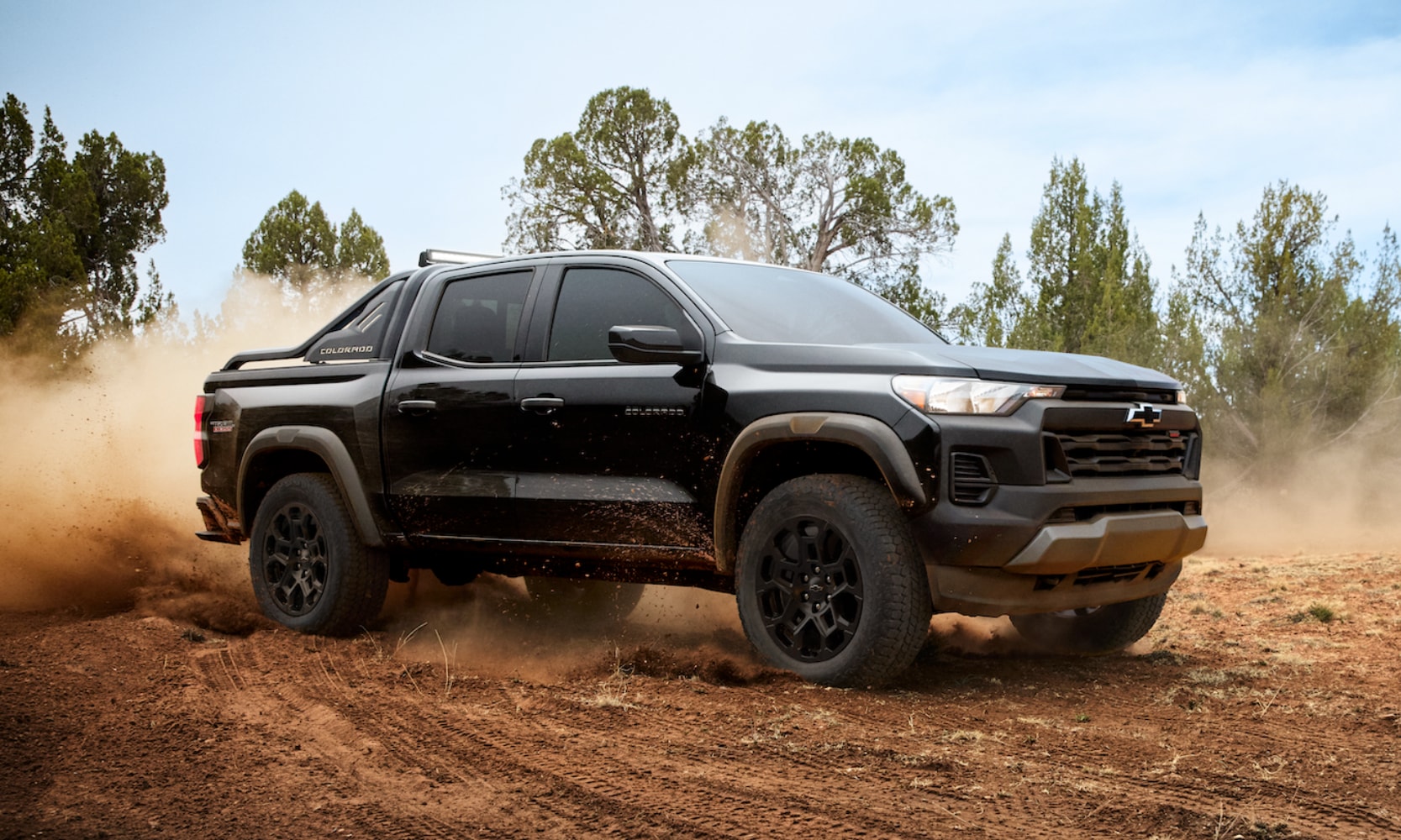 Exterior image of a black 2026 Chevy Colorado Trail Boss off-roading in a forest with dirt blowing