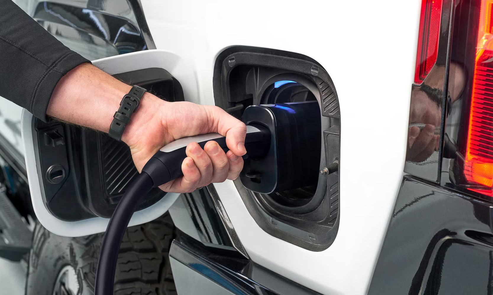 Close-up image of a person's hand charging a white 2025 GMC Hummer EV Pickup Truck