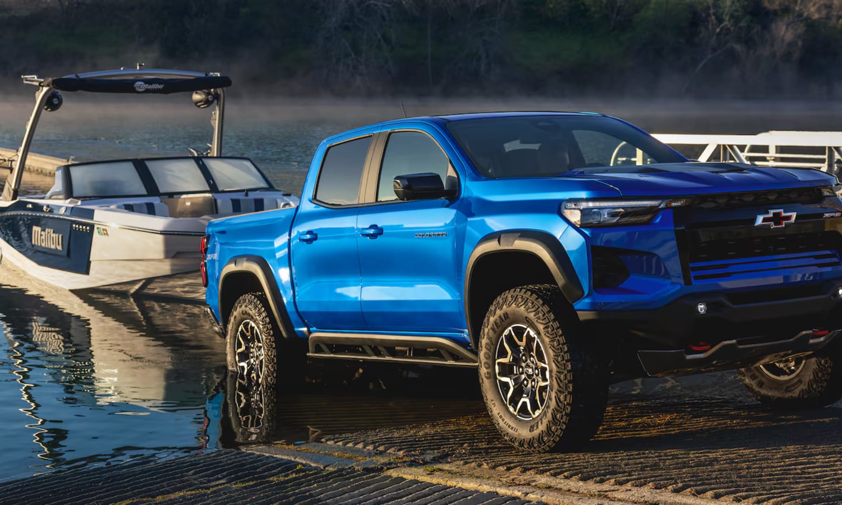 Exterior image of a blue 2026 Chevy Colorado towing a small boat from a lake onto land