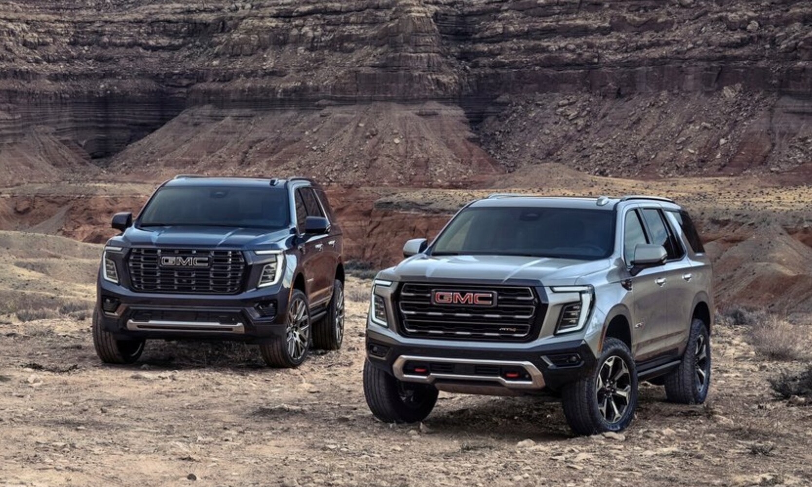 Front profile view of a 2025 GMC Yukon Denali on the left parked next to a 2025 GMC Yukon AT4 on the right