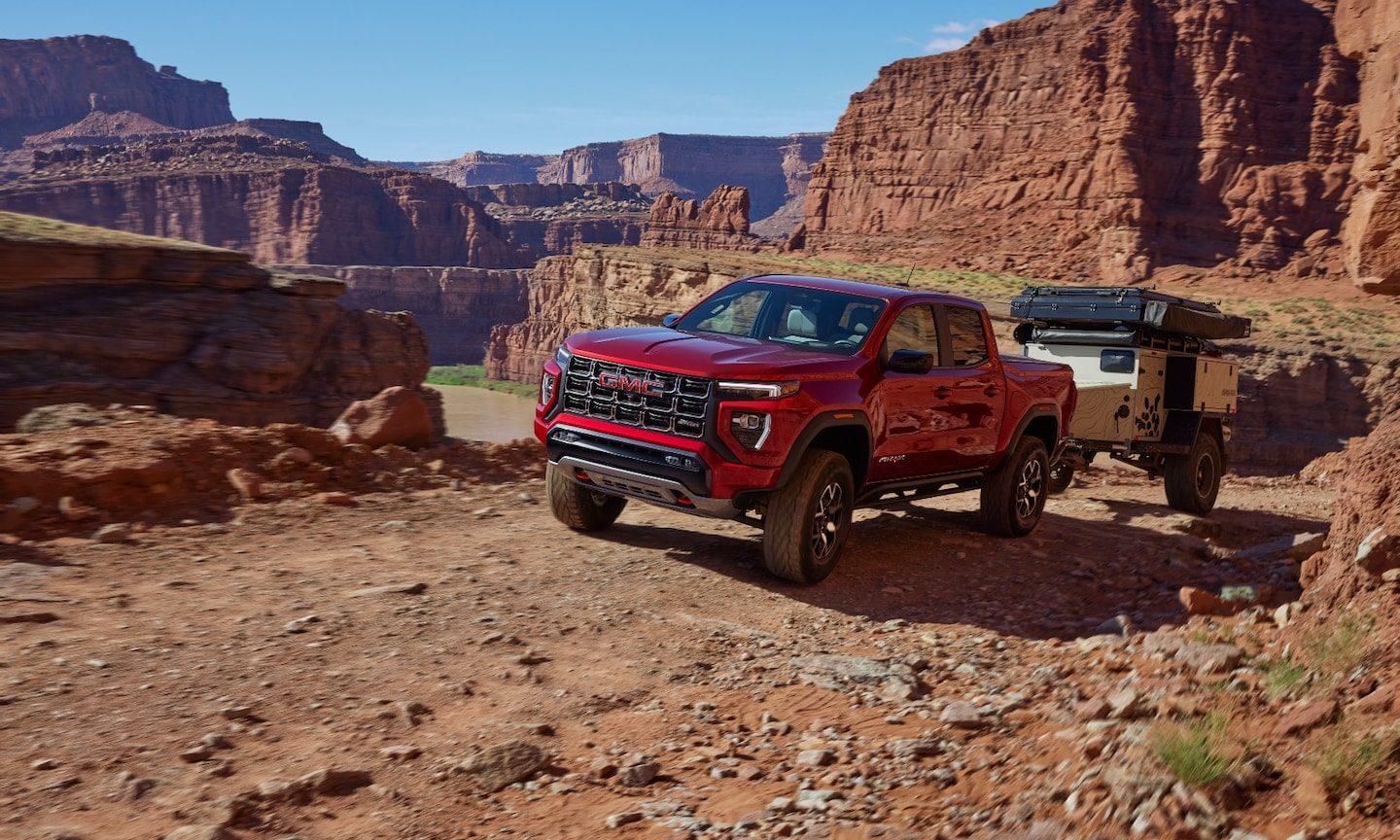 Exterior image of a red 2026 GMC Canyon AT4 towing a small trailer in a rocky mountain setting