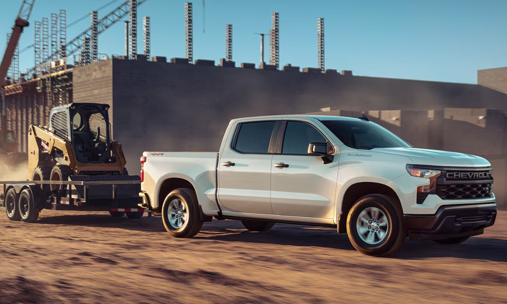 Exterior side image of a white 2025 Chevy Silverado 1500 towing an excavator in a construction zone