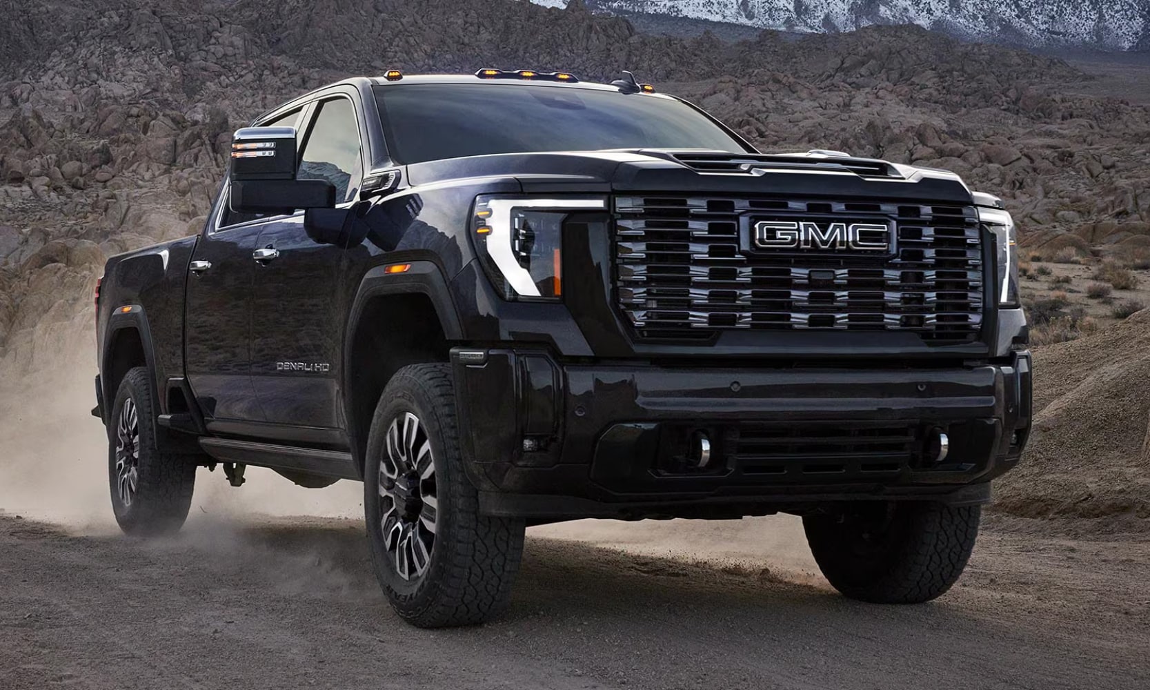 Closeup image of a black 2026 GMC Sierra HD Denali Ultimate driving on a dirt road