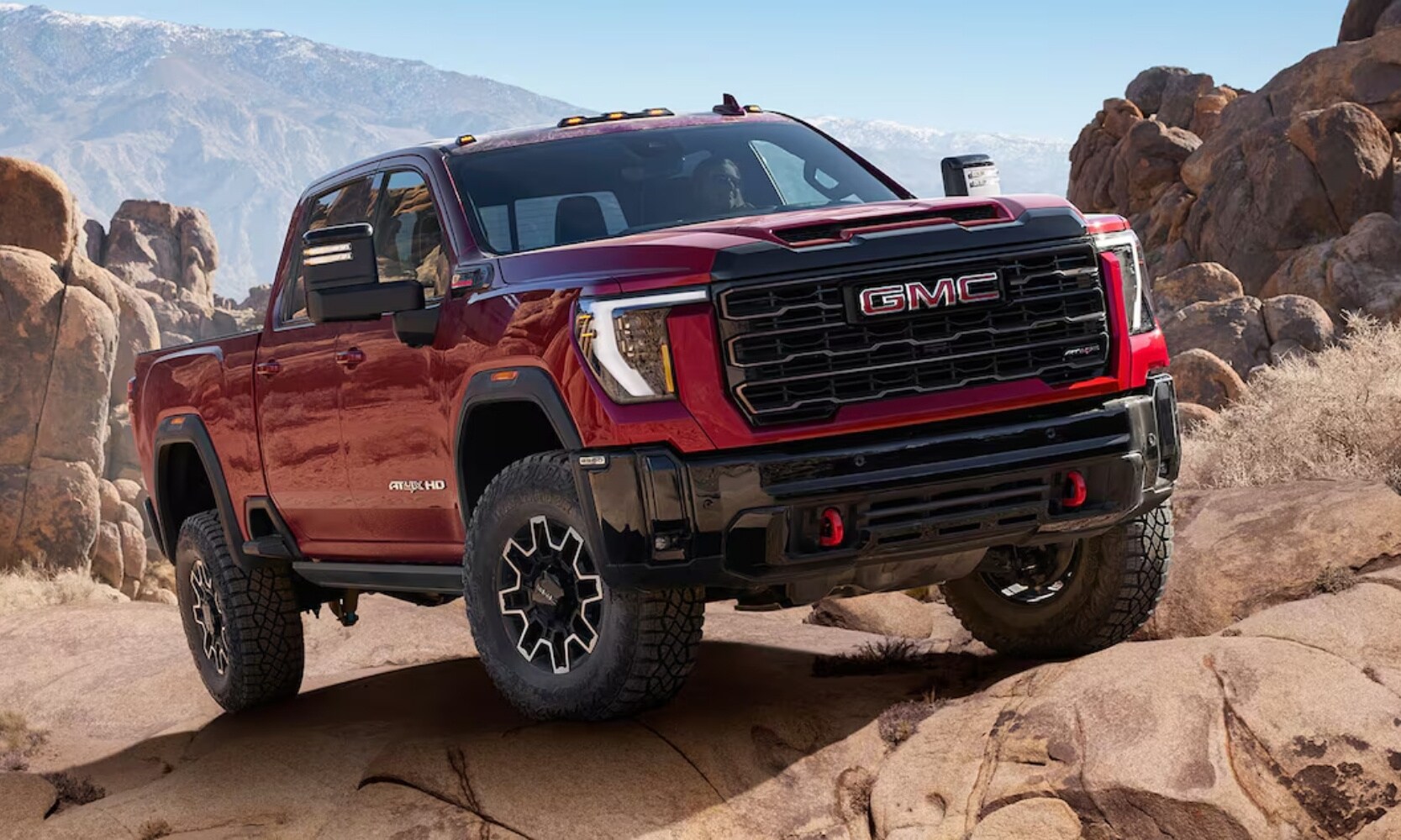 Exterior image of a red 2025 GMC Sierra 2500 HD AT4X off-roading up a rocky mountain incline