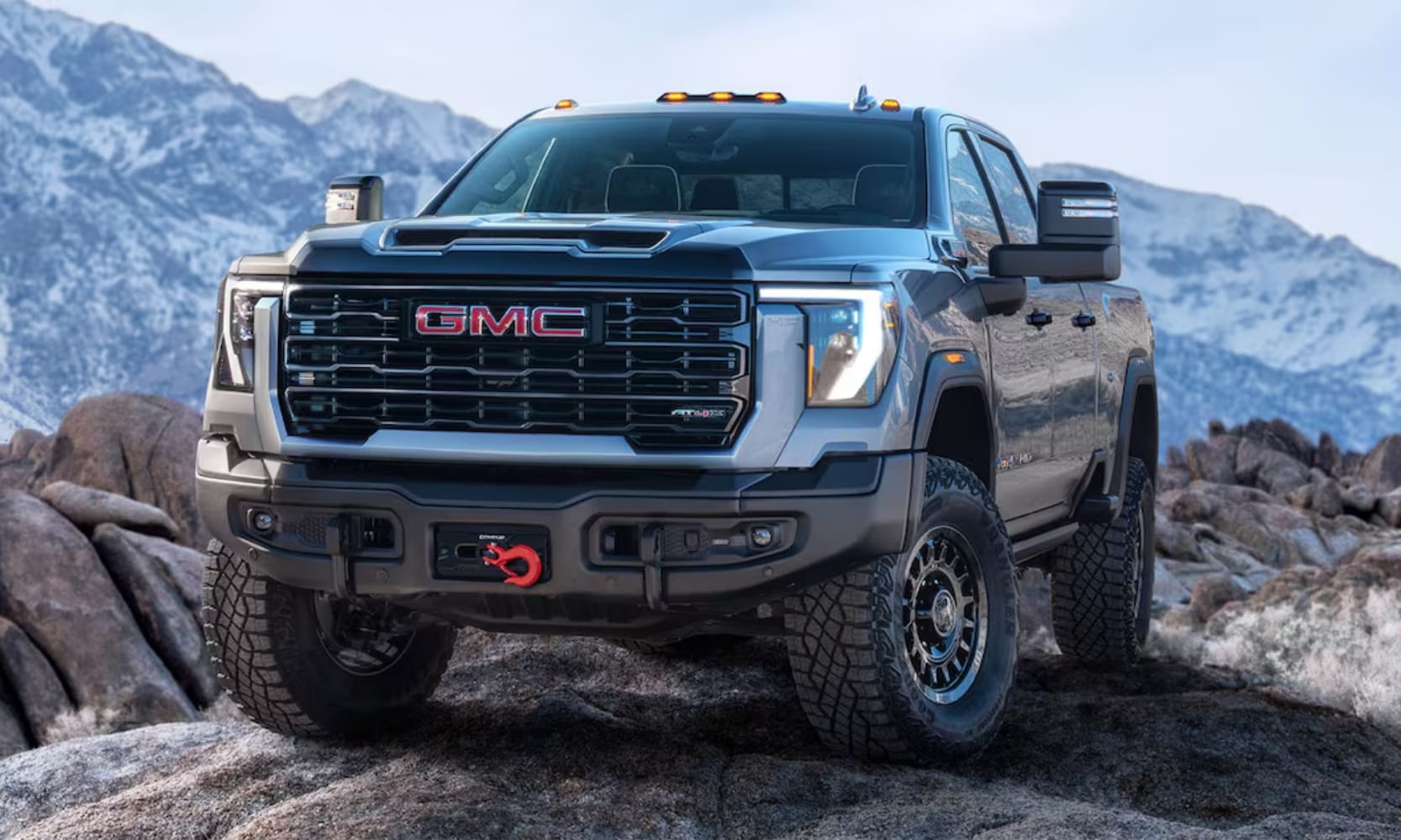 Exterior image of a light gray 2025 GMC Sierra 2500 HD AT4X AEV Edition parked on a rocky mountain