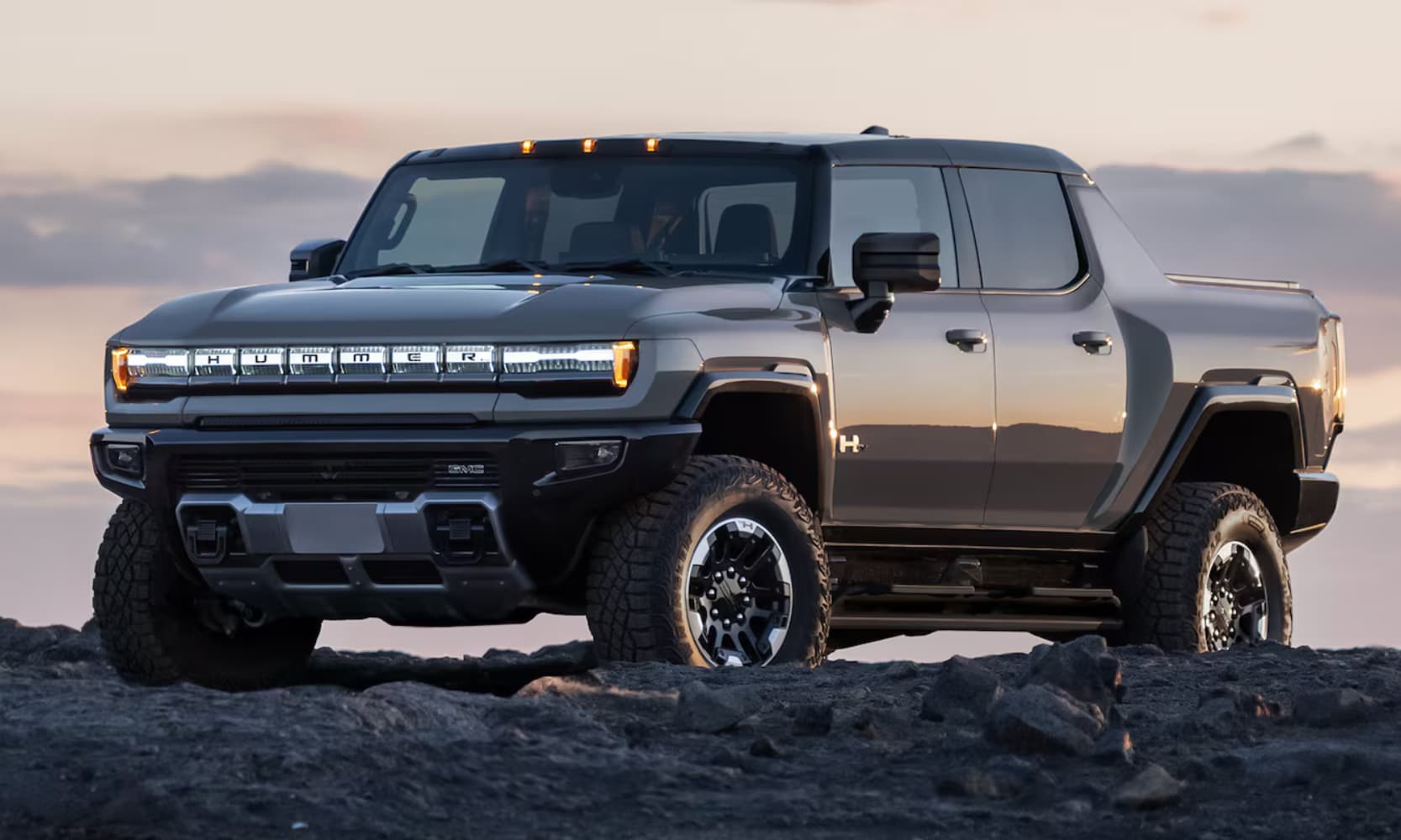 Exterior side angle image of a dark gray 2026 GMC Hummer EV Pickup parked on a rocky mountain on a cloudy day