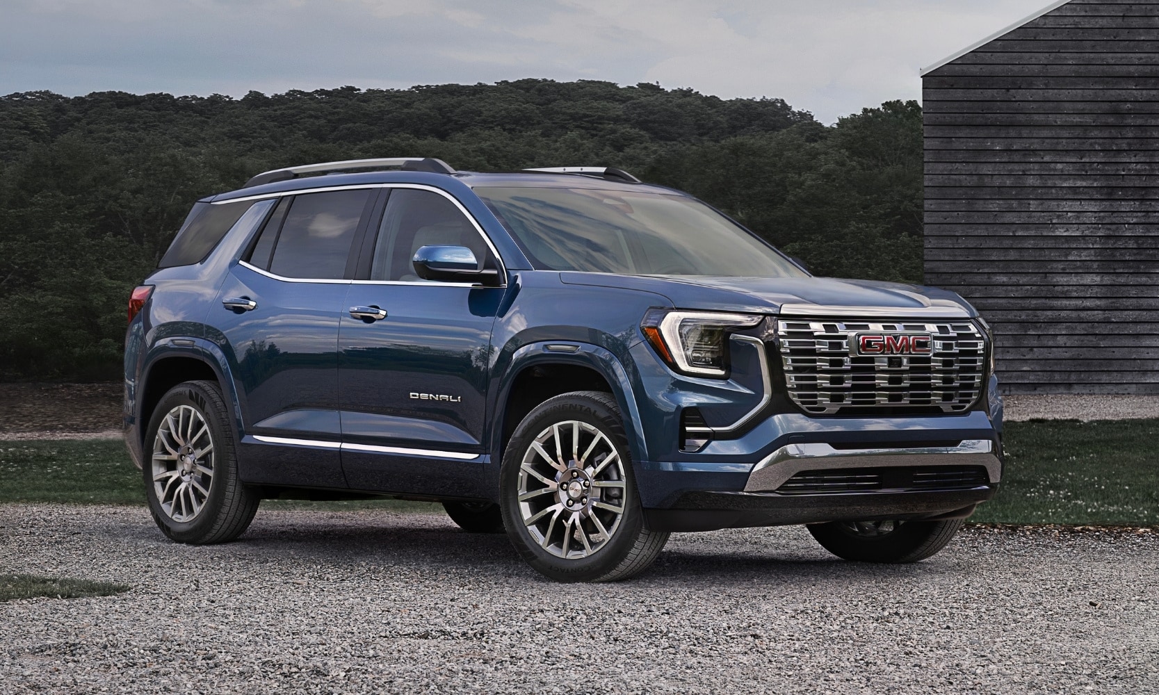 Exterior image of a blue 2026 GMC Terrain Denali parked in a rocky driveway