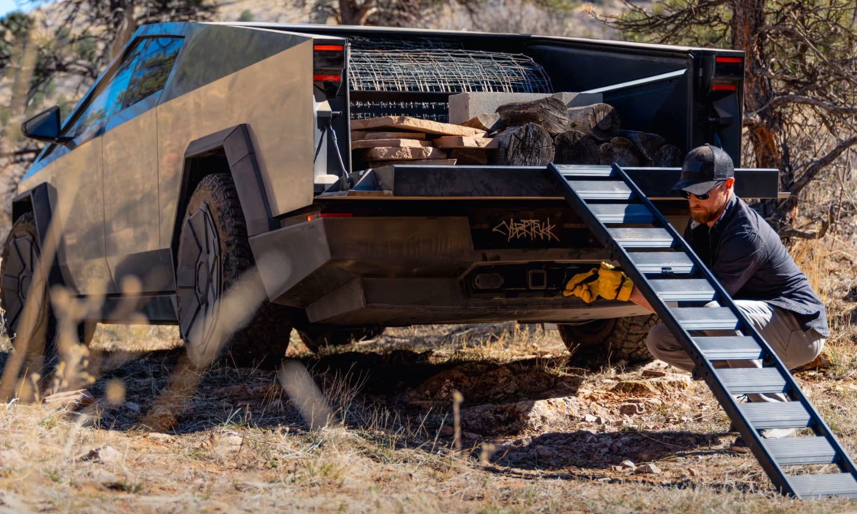 Exterior rear-view image of a person loading cargo on the 2025 Tesla Cybertruck trunk with its tailgate ramp out
