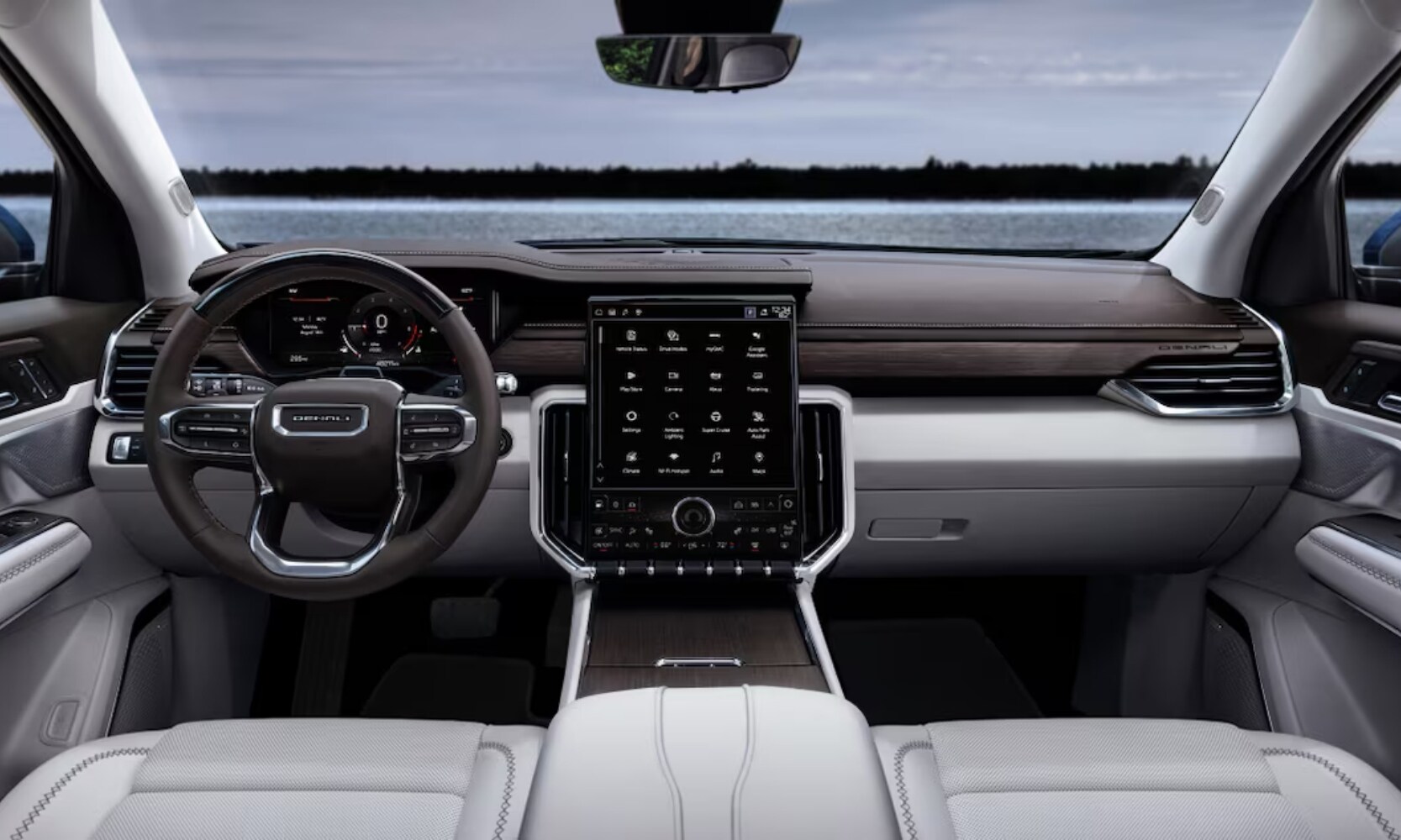 Interior image of the 2025 GMC Acadia front seating area, infotainment screen, and dashboard with lakefront views in the windshield