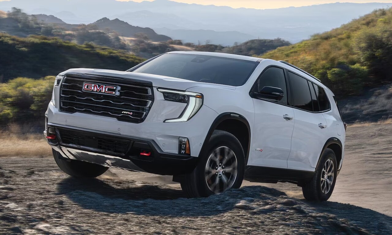 Exterior image of a white 2026 GMC Acadia driving up a rocky hill in a mountainous setting