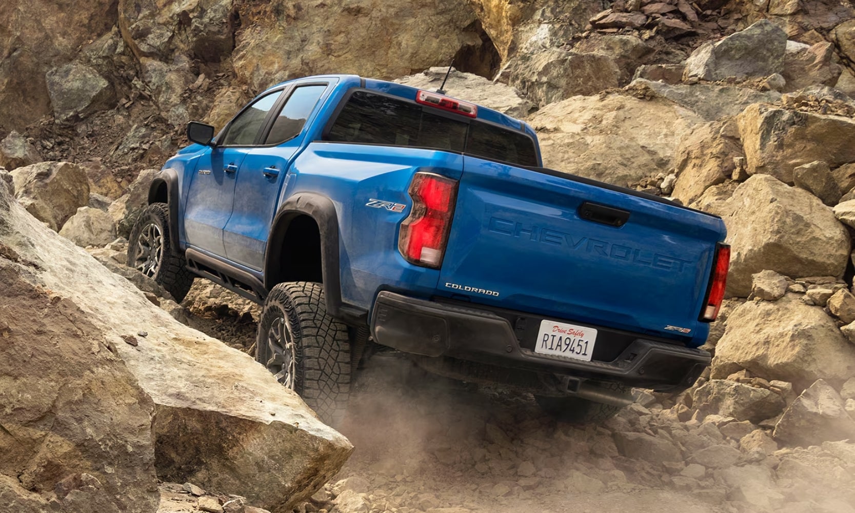 Exterior rear image of a blue 2024 Chevy Colorado ZR2 off-roading up a steep rocky incline