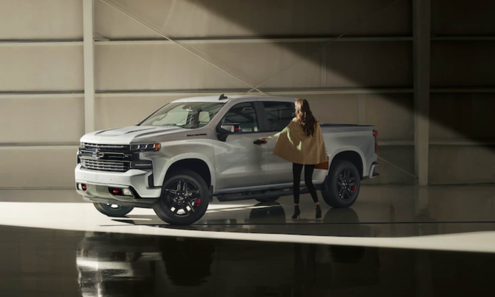 Exterior image of a person entering a white 2021 Chevy Silverado 1500 in a warehouse setting