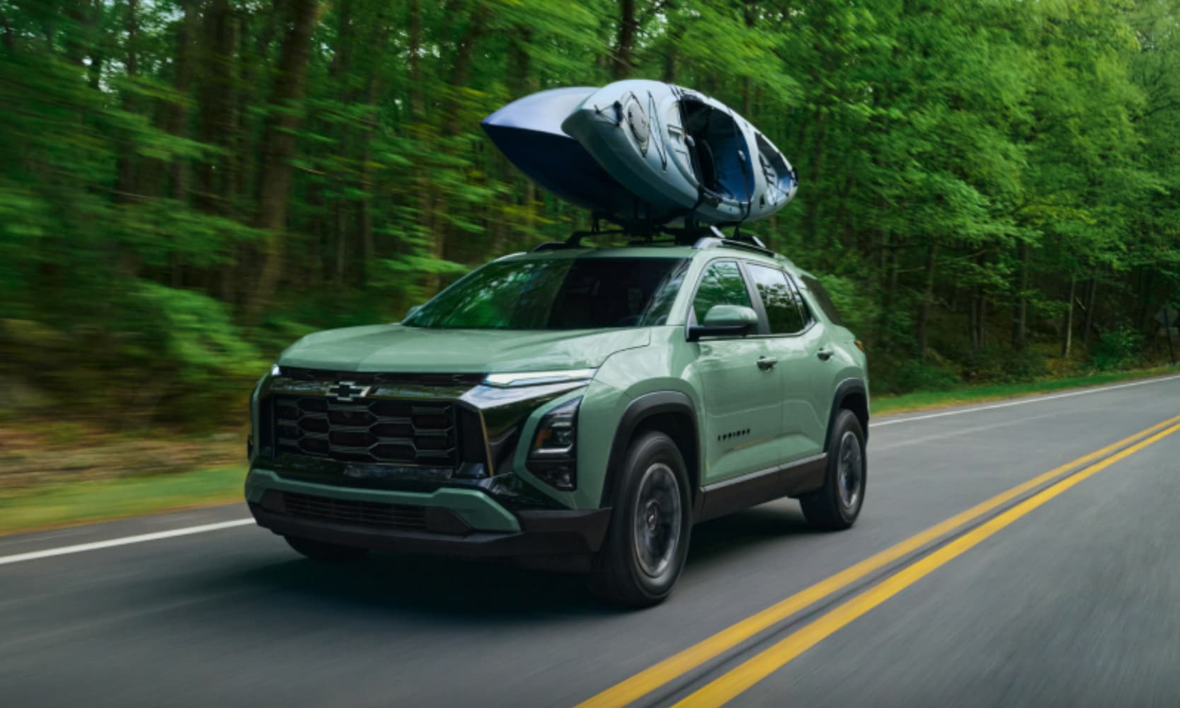 Exterior image of a light green 2026 Chevrolet Equinox ACTIV towing a kayak on an open a forest-lined freeway