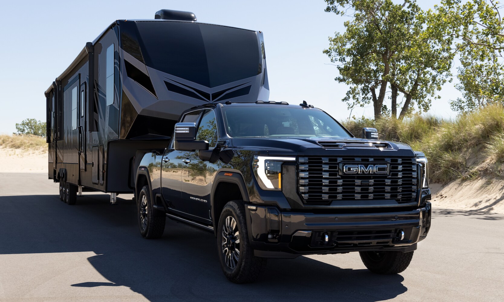 Exterior image of a black 2026 GMC Sierra HD 2500 towing a camping trailer in a coastal setting