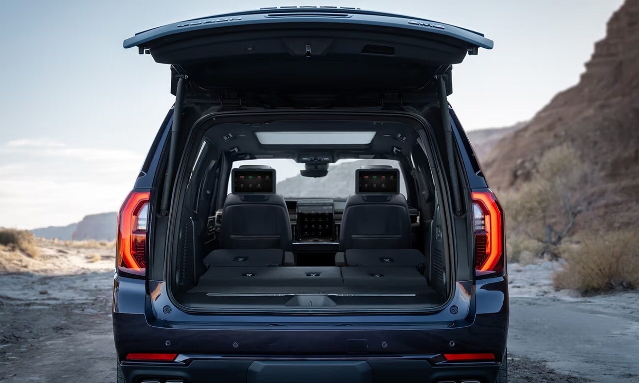 Exterior rear image of a blue 2026 GMC Yukon open trunk in a coastal setting