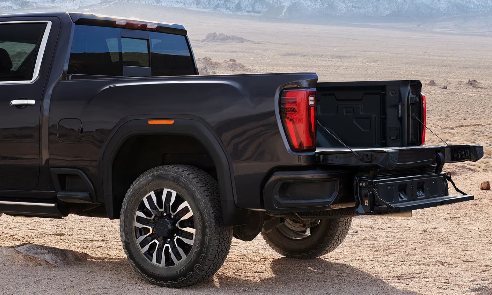 Close-up exterior side image of a black 2026 GMC Sierra HD MultiPro Tailgate with it open in a mountain landscape